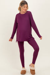 woman wearing a dark purple maternity top and matching leggings, showing her baby bump, paired with brown fuzzy slippers