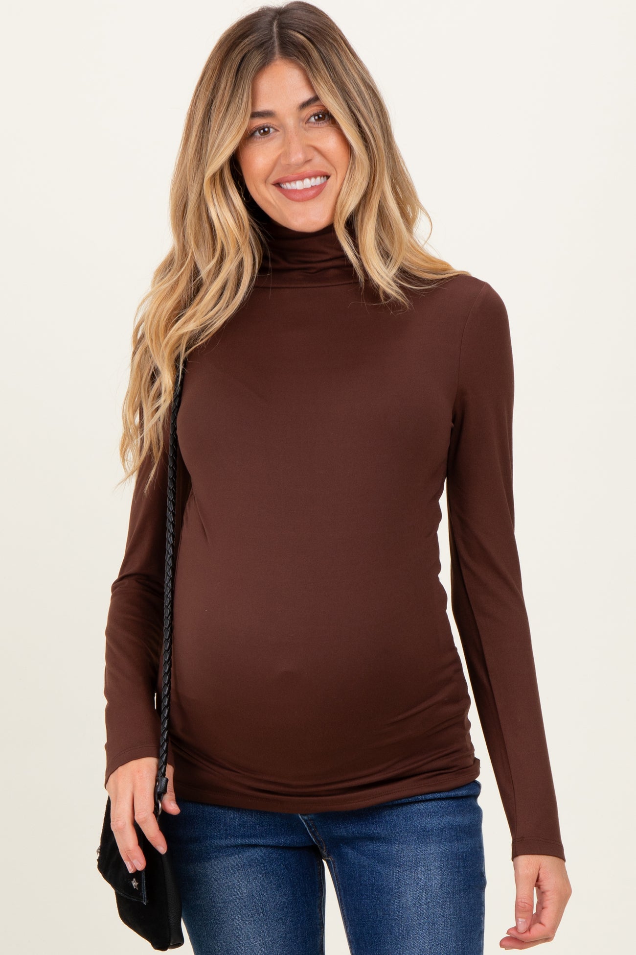 woman wearing a brown long sleeve turtleneck maternity top and showing her baby bump