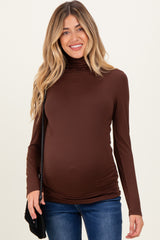 woman wearing a brown long sleeve turtleneck maternity top and showing her baby bump