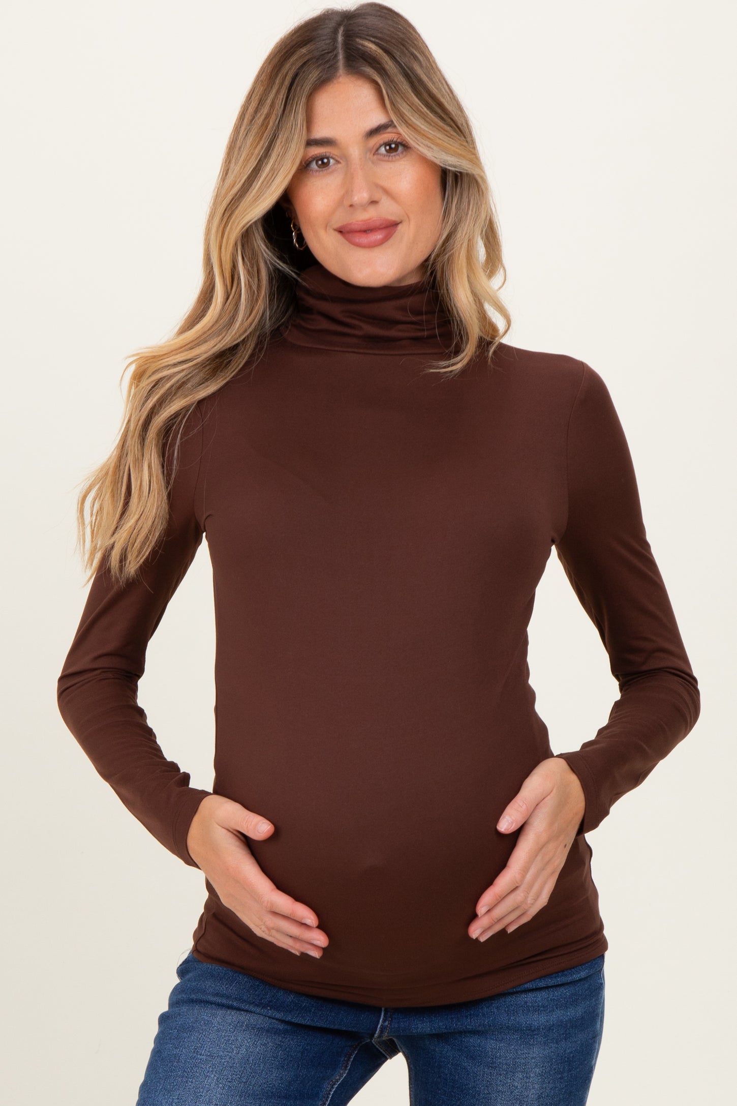 woman wearing a brown long sleeve maternity top and holding her baby bump