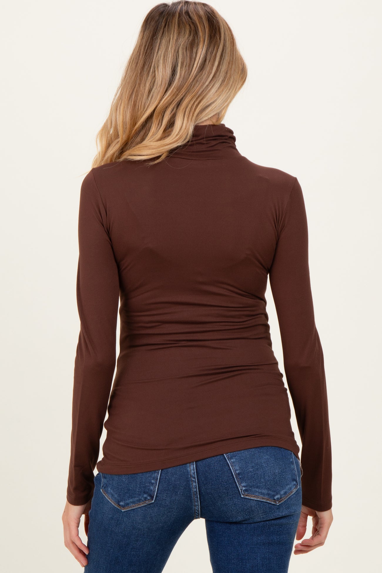 woman wearing a brown long sleeve maternity top with a fitted silhouette and ruching details at the sides