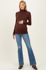 woman wearing a brown long sleeve maternity turtleneck top and flared jeans, holding her baby bump