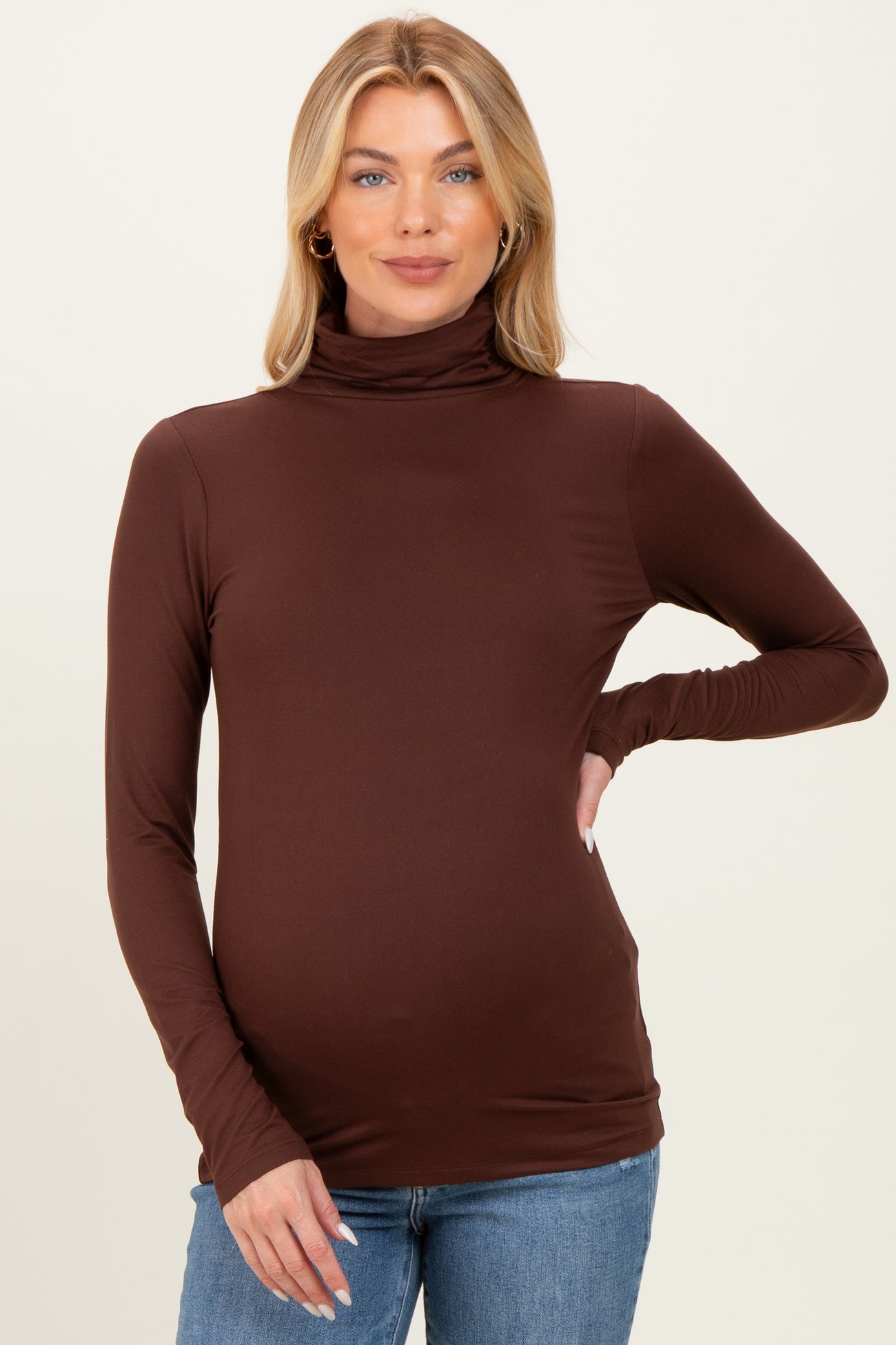 woman wearing a brown long sleeve maternity turtleneck top and showing her baby bump