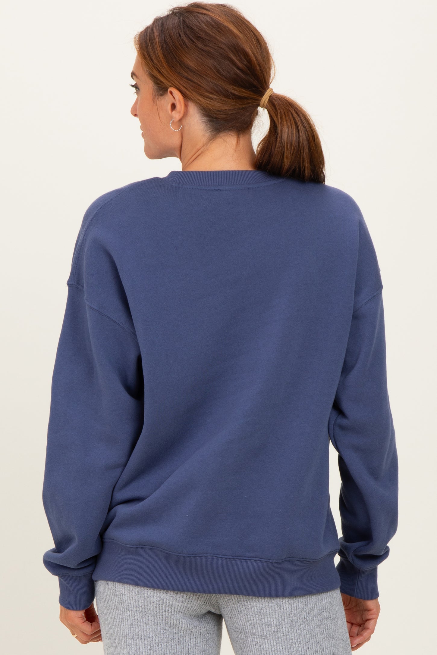 woman wearing a navy blue oversized sweatshirt, shown from the back, styled with gray sweatpants