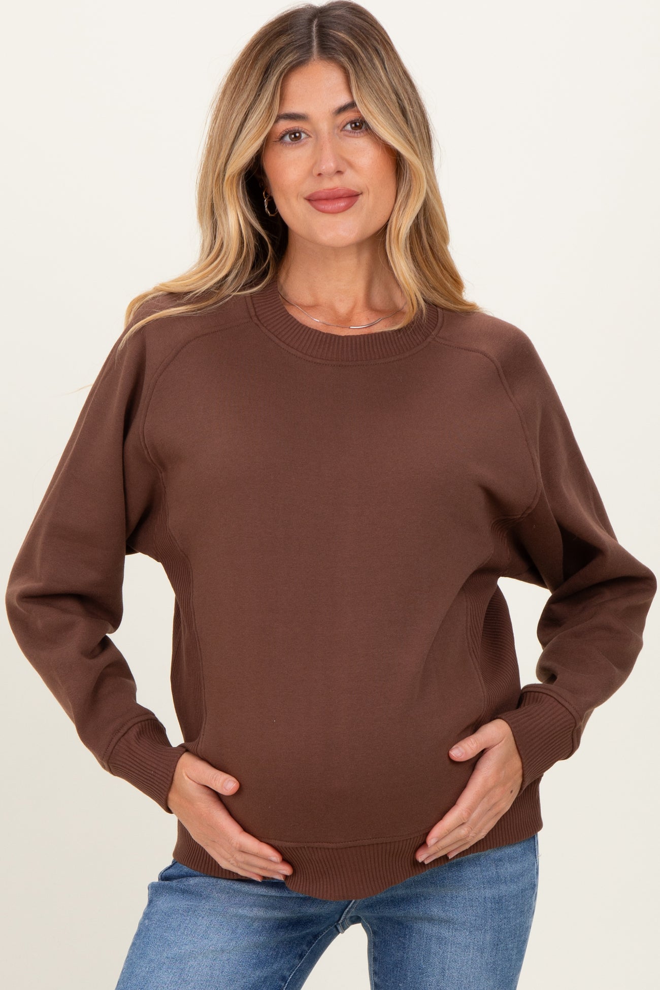 woman wearing a brown maternity sweatshirt with a relaxed fit and long sleeves, holding her baby bump