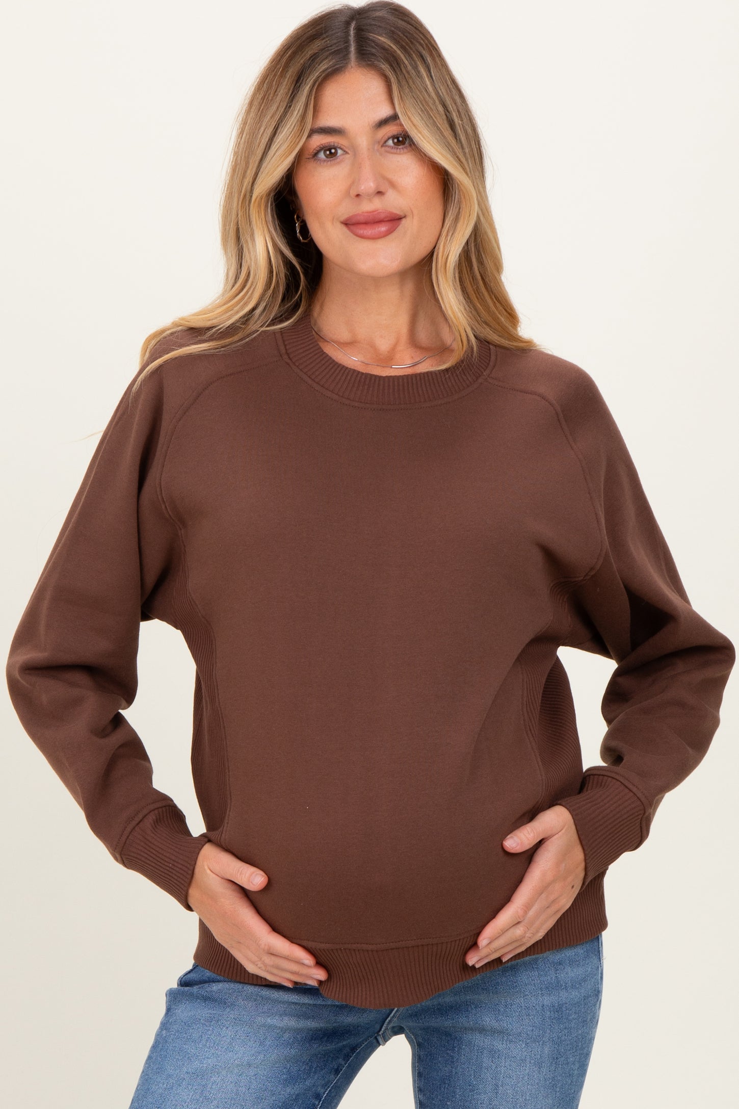 woman wearing a brown maternity sweatshirt with a relaxed fit and long sleeves, holding her baby bump