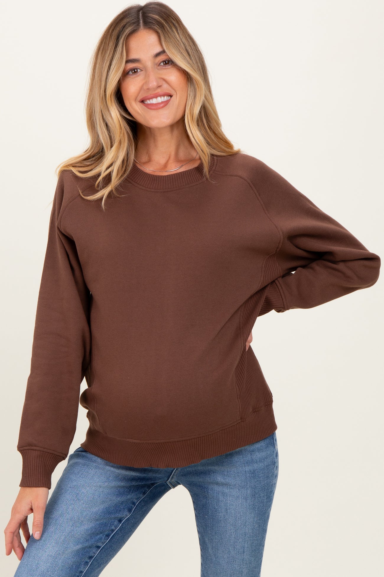 woman wearing a brown maternity sweatshirt paired with blue jeans and showing her baby bump
