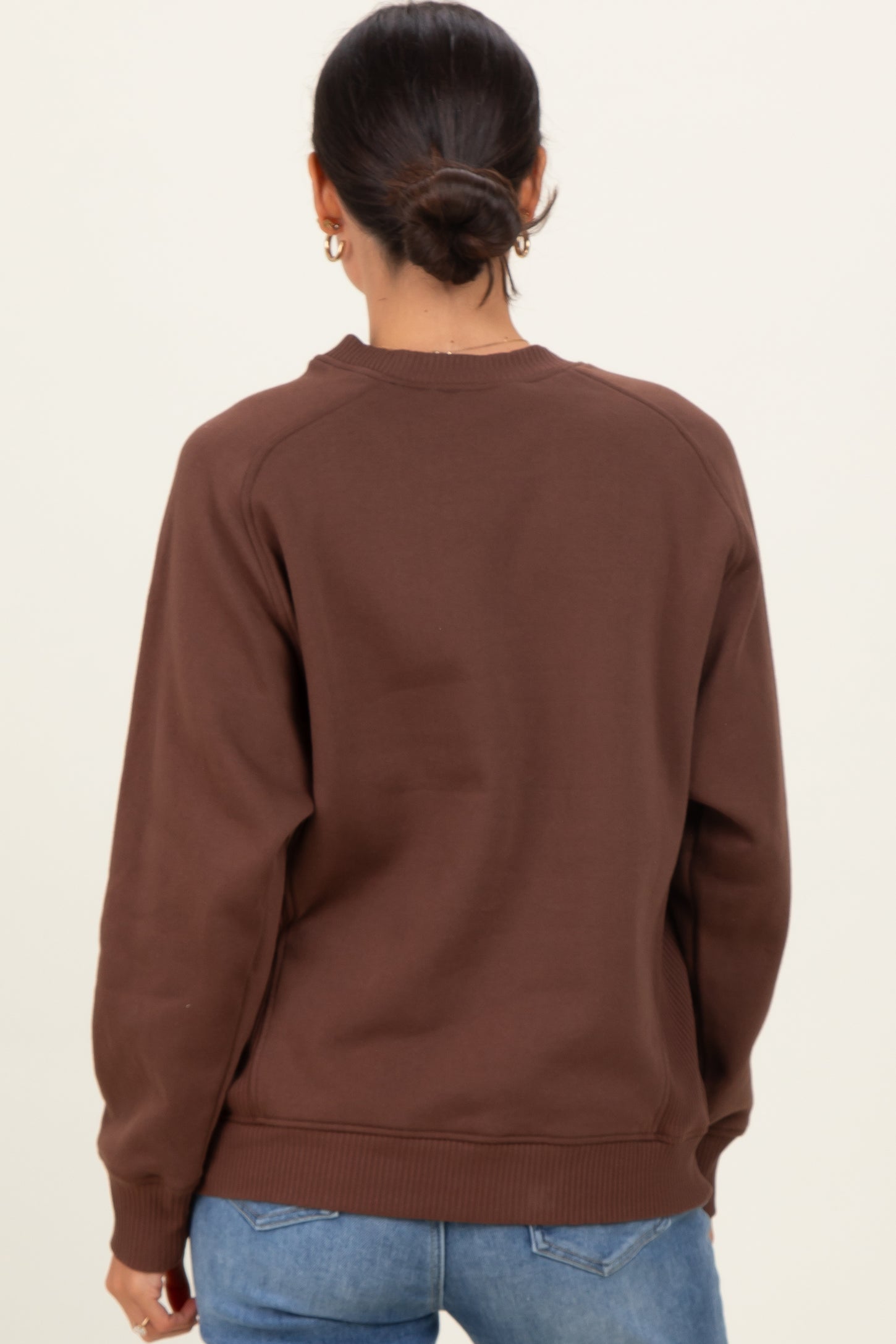 woman wearing a brown oversized sweatshirt with a crew neckline and raglan sleeves