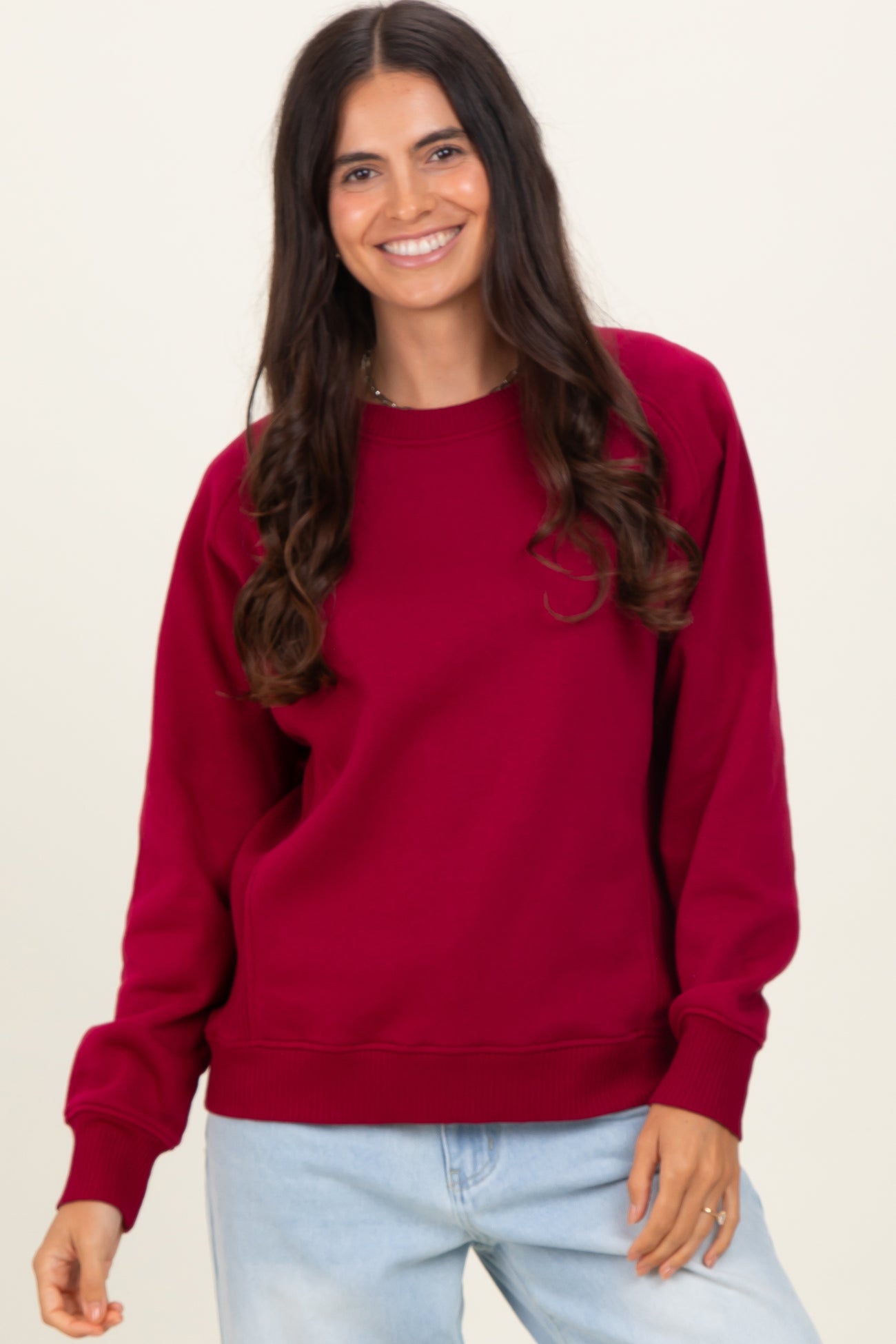 woman wearing a burgundy sweatshirt with a relaxed fit and ribbed cuffs, smiling at the camera