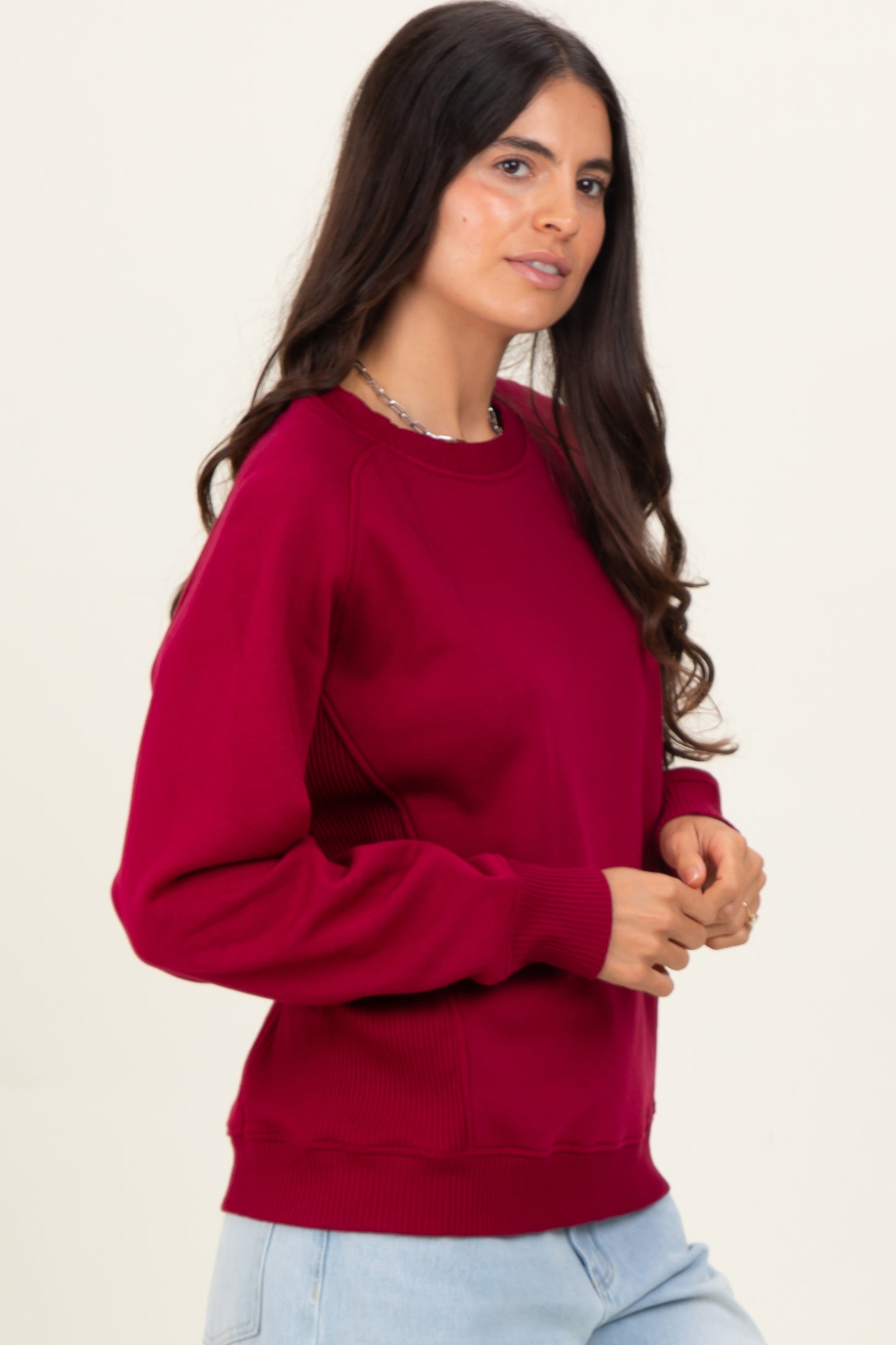 woman wearing a burgundy crewneck sweatshirt with ribbed detailing and relaxed fit