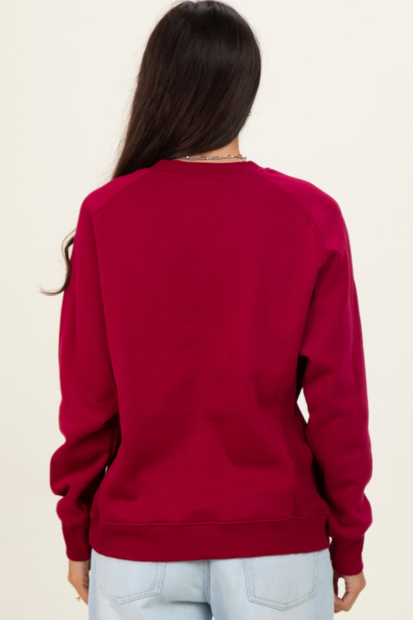 woman wearing a burgundy long sleeve sweatshirt, viewed from the back, with raglan sleeves and ribbed cuffs