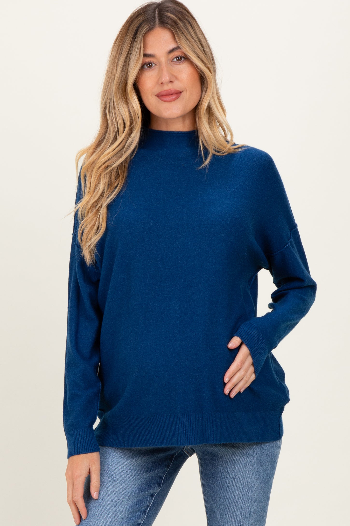 woman wearing a dark blue maternity sweater with a high neckline and relaxed fit, showing her baby bump