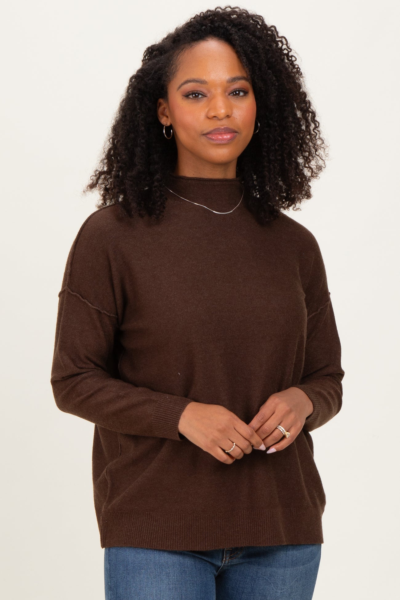woman wearing a dark brown long sleeve sweater with a high neckline and relaxed fit, styled with light blue jeans