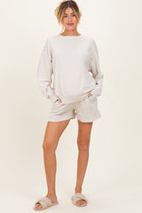 woman wearing a light beige maternity sweatshirt and matching shorts, standing with hands in pockets and wearing slippers