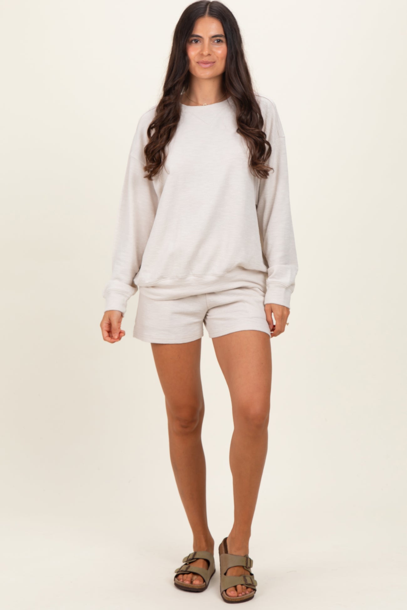 woman wearing a light beige long sleeve sweatshirt and matching shorts, standing in a relaxed pose