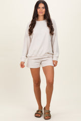 woman wearing a light beige long sleeve sweatshirt and matching shorts, standing in a relaxed pose