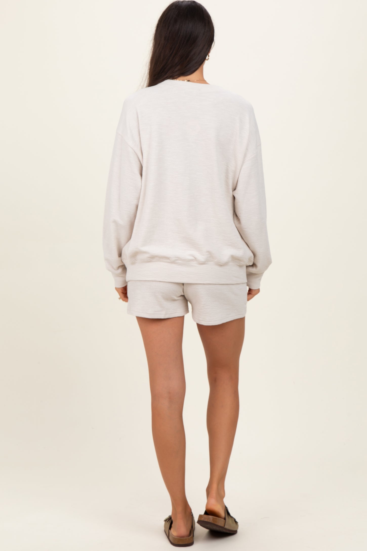 woman wearing a light gray oversized sweatshirt and matching shorts, shown from the back