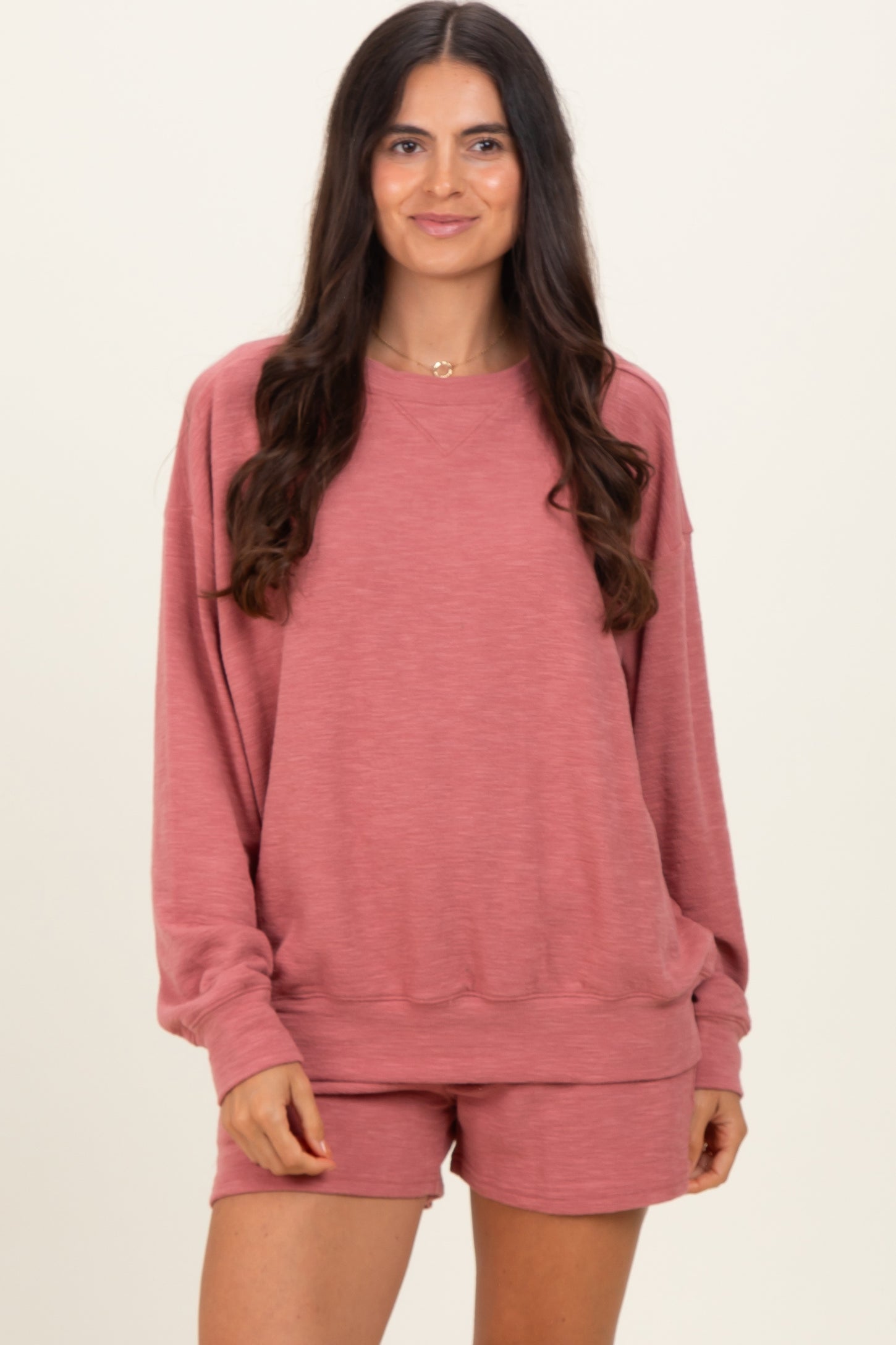woman wearing a rose-colored oversized sweatshirt and matching shorts, smiling at the camera