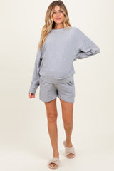 woman wearing a light gray maternity loungewear set with a loose sweatshirt and matching shorts, showing her baby bump