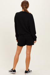 woman wearing a black oversized sweatshirt and matching black shorts, standing with her back to the camera