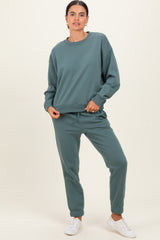 woman wearing a green long sleeve sweatshirt and matching sweatpants, standing with one hand on her hip