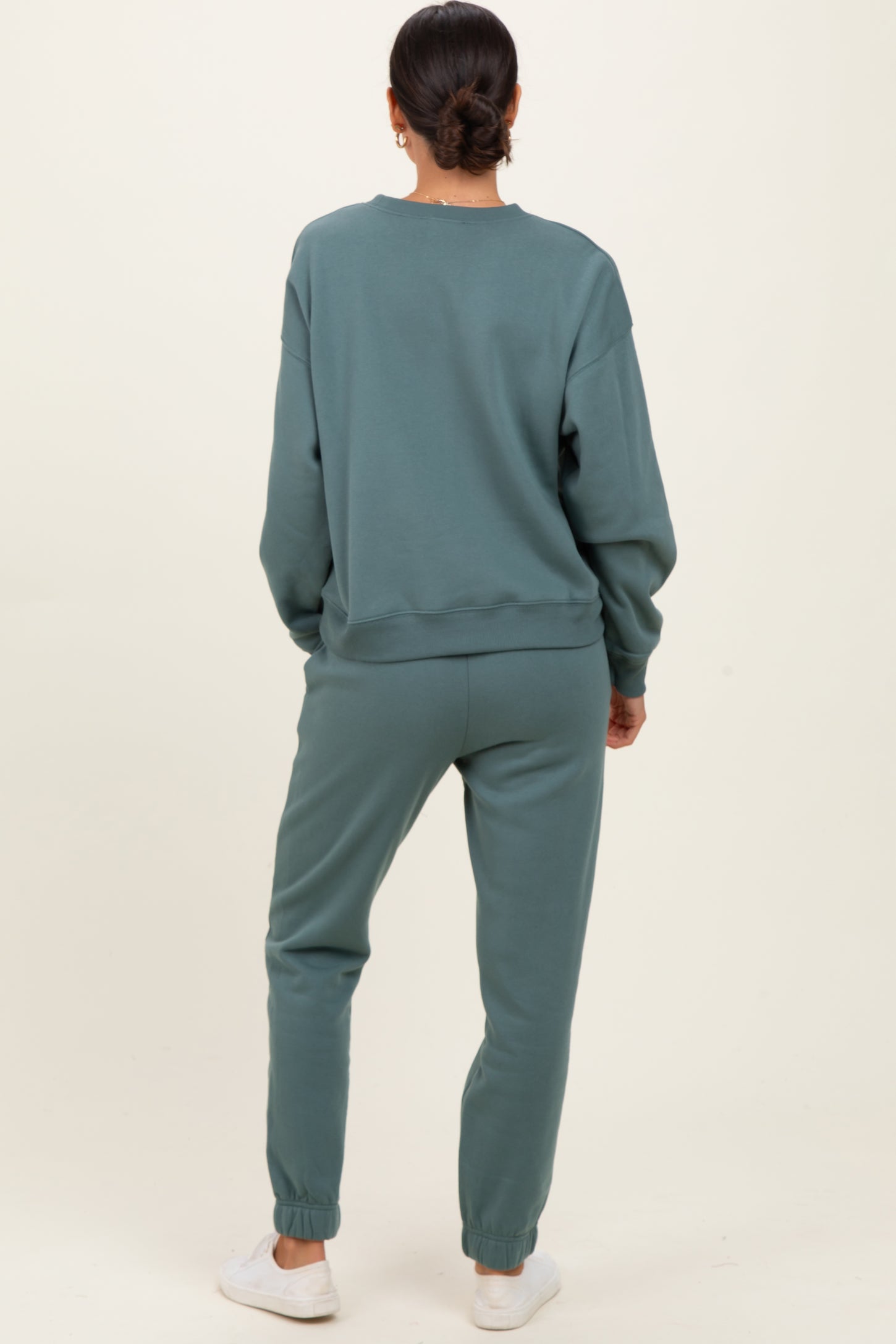 woman wearing a relaxed fit teal sweatshirt and matching joggers, standing with her back to the camera