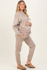 woman wearing a beige maternity sweatshirt and joggers with pockets and a baby bump visible