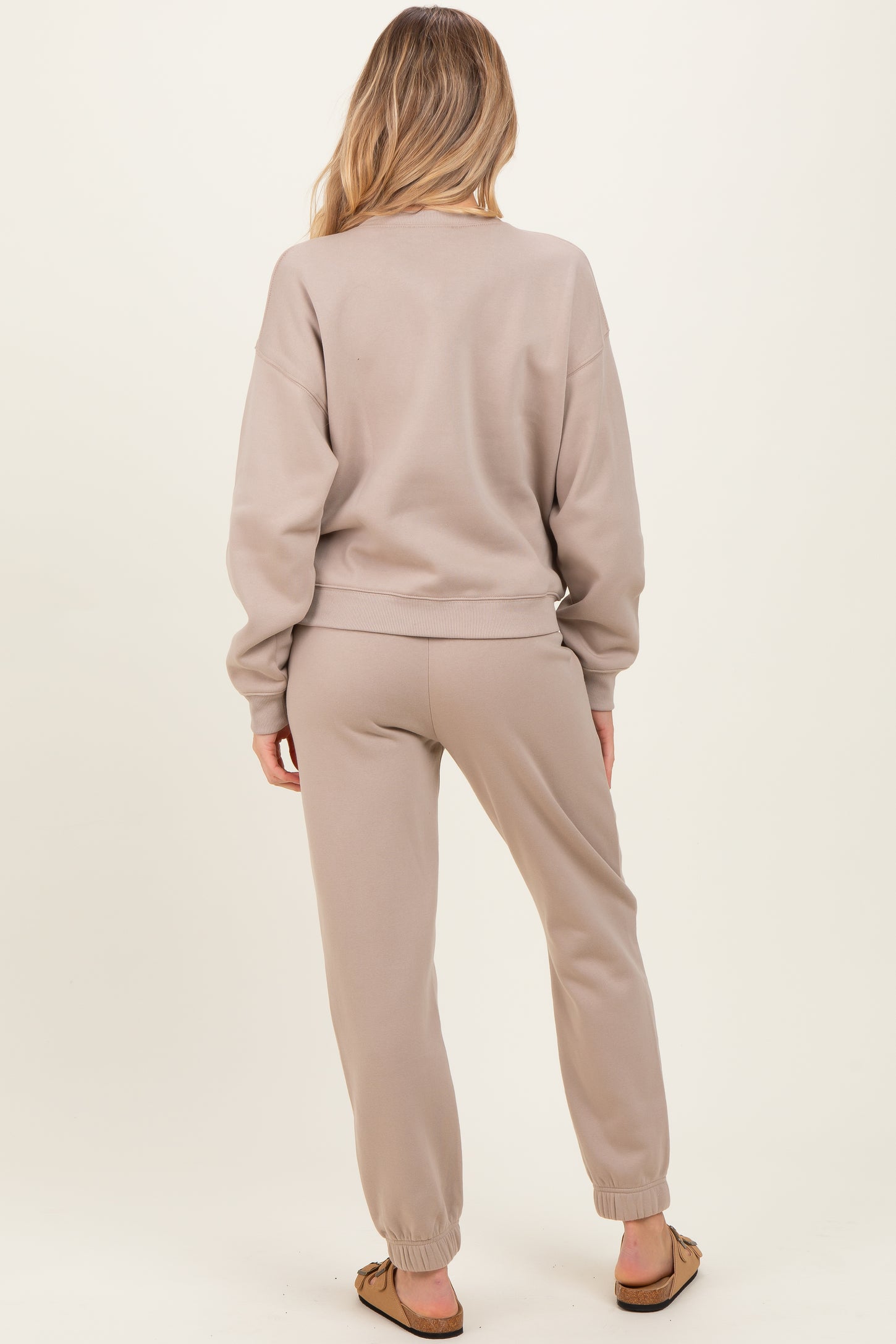 woman wearing a beige maternity sweatshirt and matching joggers, showing the back view