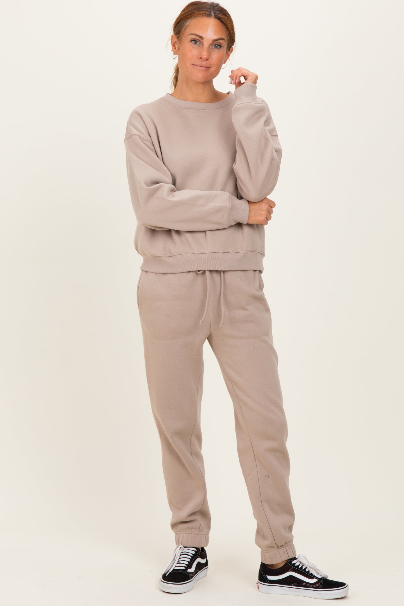 woman wearing a beige oversized sweatshirt and matching joggers, styled with black sneakers