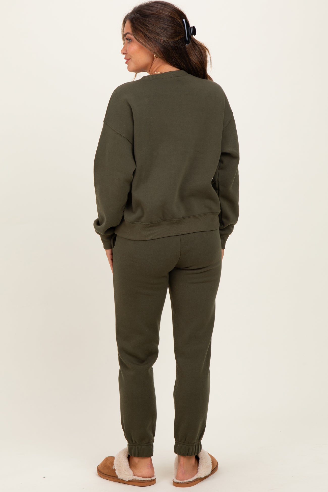 woman wearing a dark olive green maternity sweatsuit standing with back to the camera