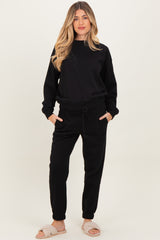 woman wearing a black maternity loungewear set with a relaxed fit sweatshirt and jogger pants, enjoying comfort at home