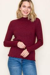 woman wearing a burgundy ribbed long sleeve top with scalloped edges and standing with a smile