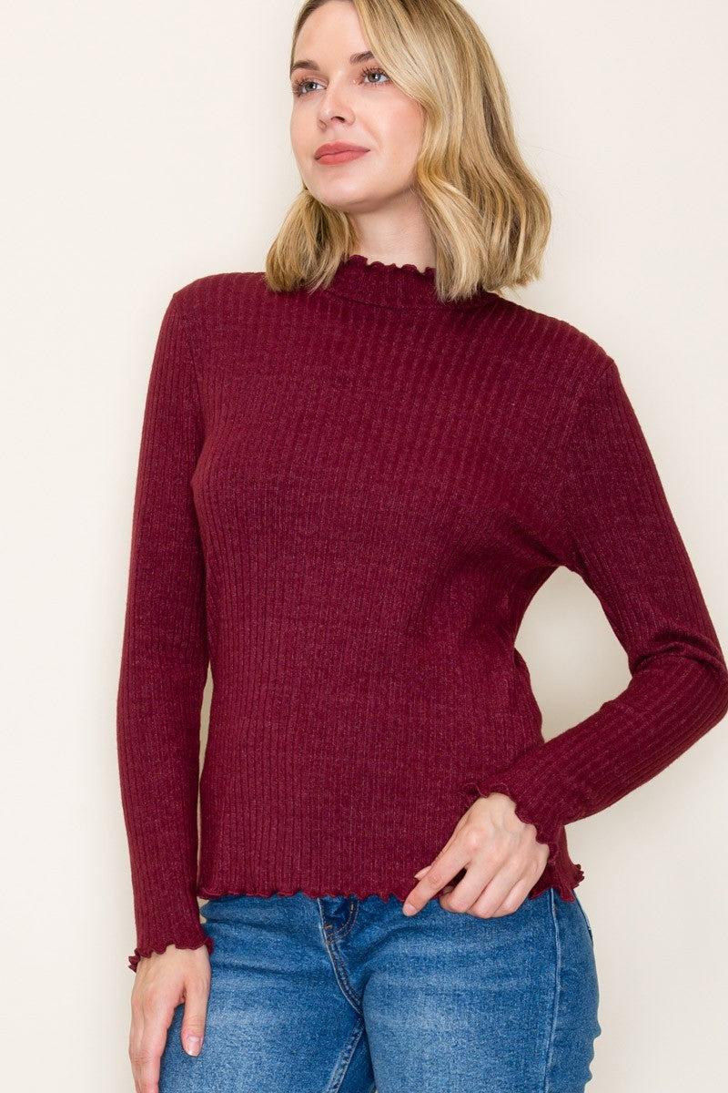 woman wearing a burgundy long sleeve ribbed top with a scalloped neckline and hem, paired with blue jeans