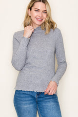 woman wearing a gray ribbed long sleeve top with scalloped edges and smiling at the camera
