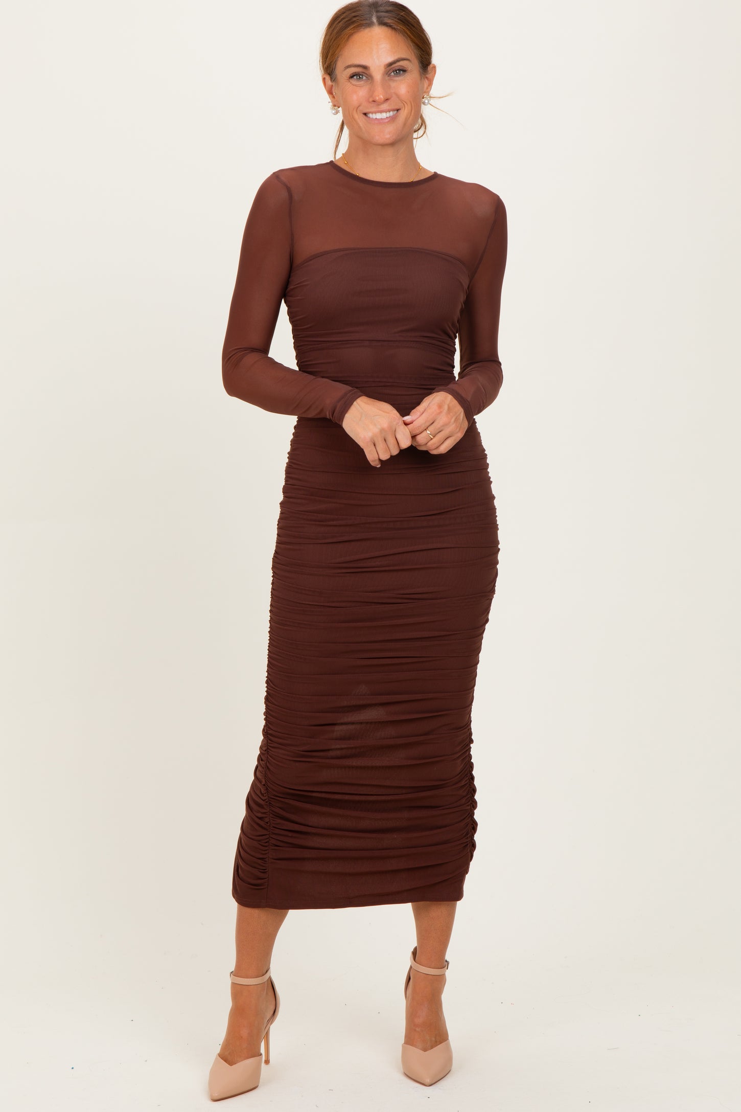 woman wearing a chocolate brown long sleeve ruched midi dress with a sheer bodice and fitted silhouette