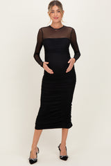 woman wearing a black maternity dress with sheer long sleeves and ruching, holding her baby bump