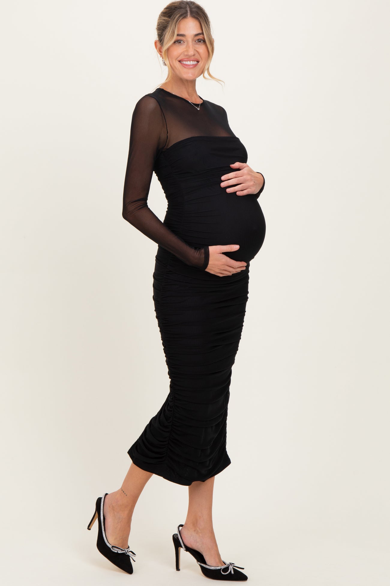 woman wearing a black maternity dress with long sheer sleeves and ruching, holding her baby bump