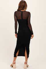 woman wearing a black ruched midi dress with long sheer sleeves and a back slit, showing the back view