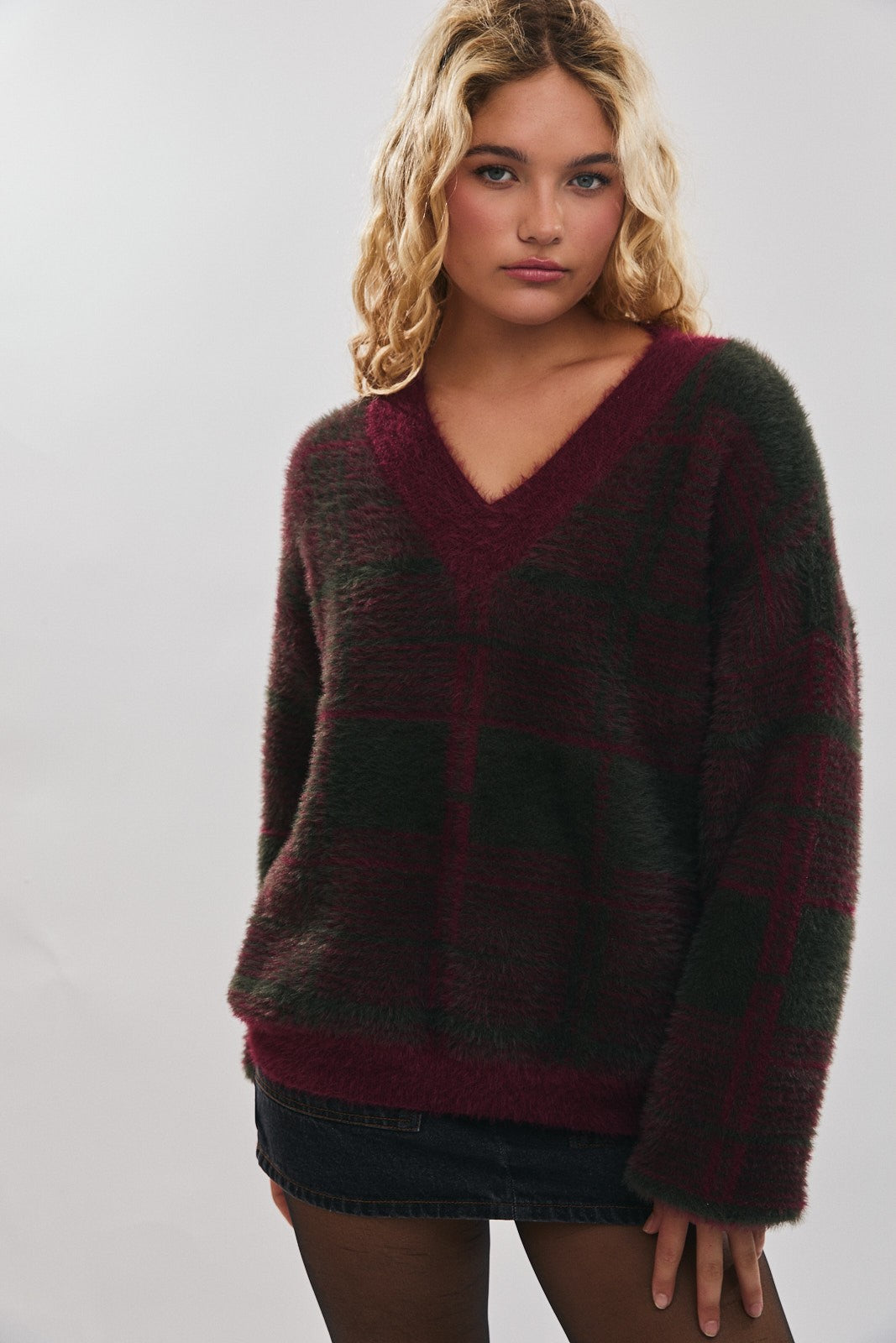 woman wearing a burgundy and green checkered oversized v-neck sweater paired with a black mini skirt