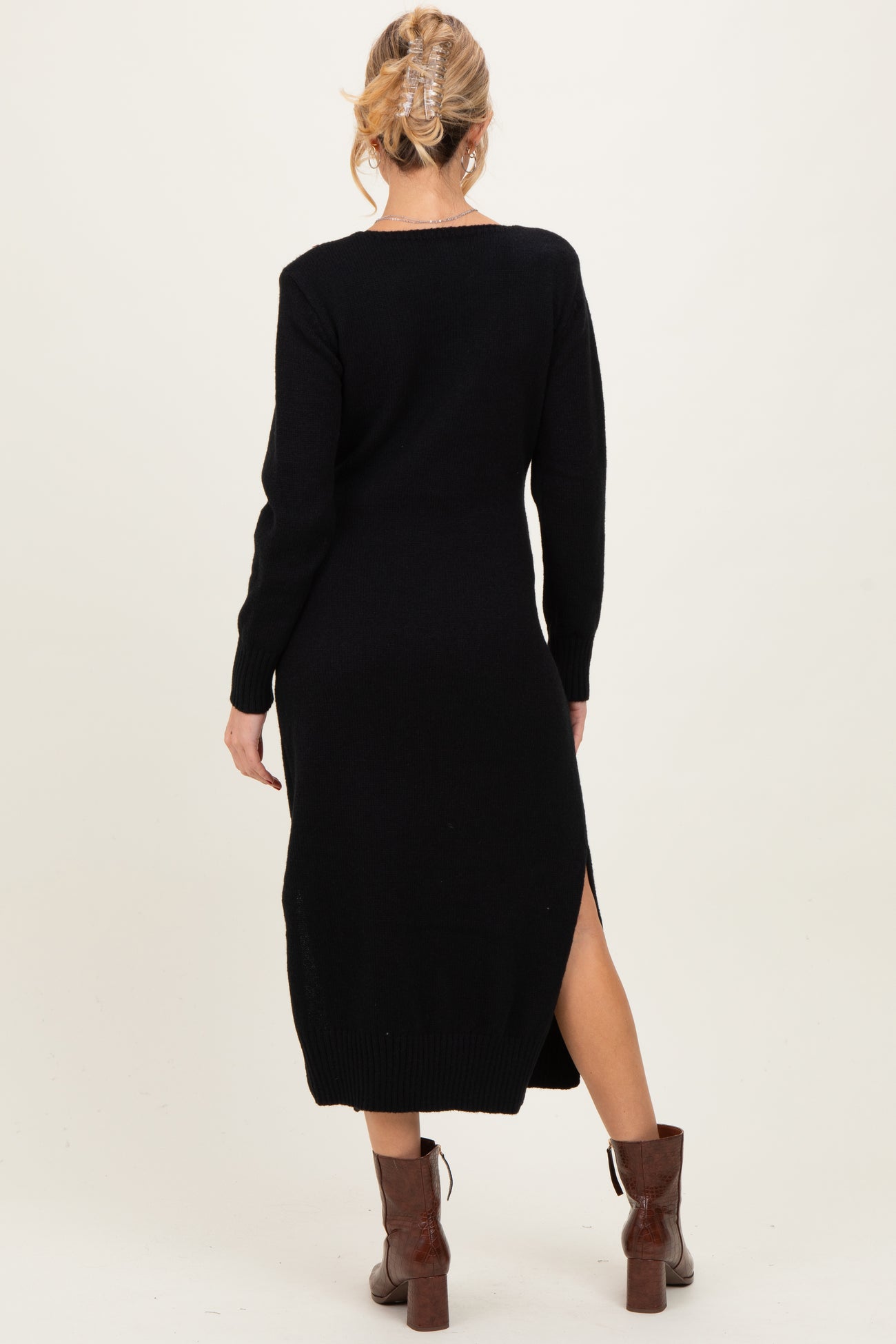 woman wearing a black maternity sweater dress with side slits and long sleeves, styled with brown heeled boots