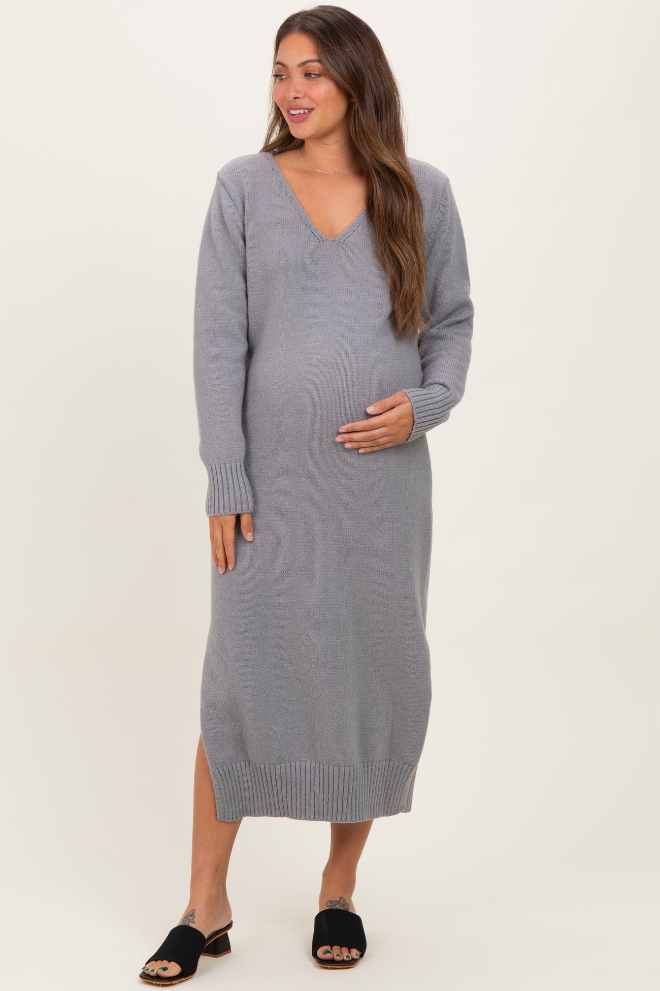 woman wearing a gray long sleeve maternity dress with a v-neck and side slits, gently cradling her baby bump