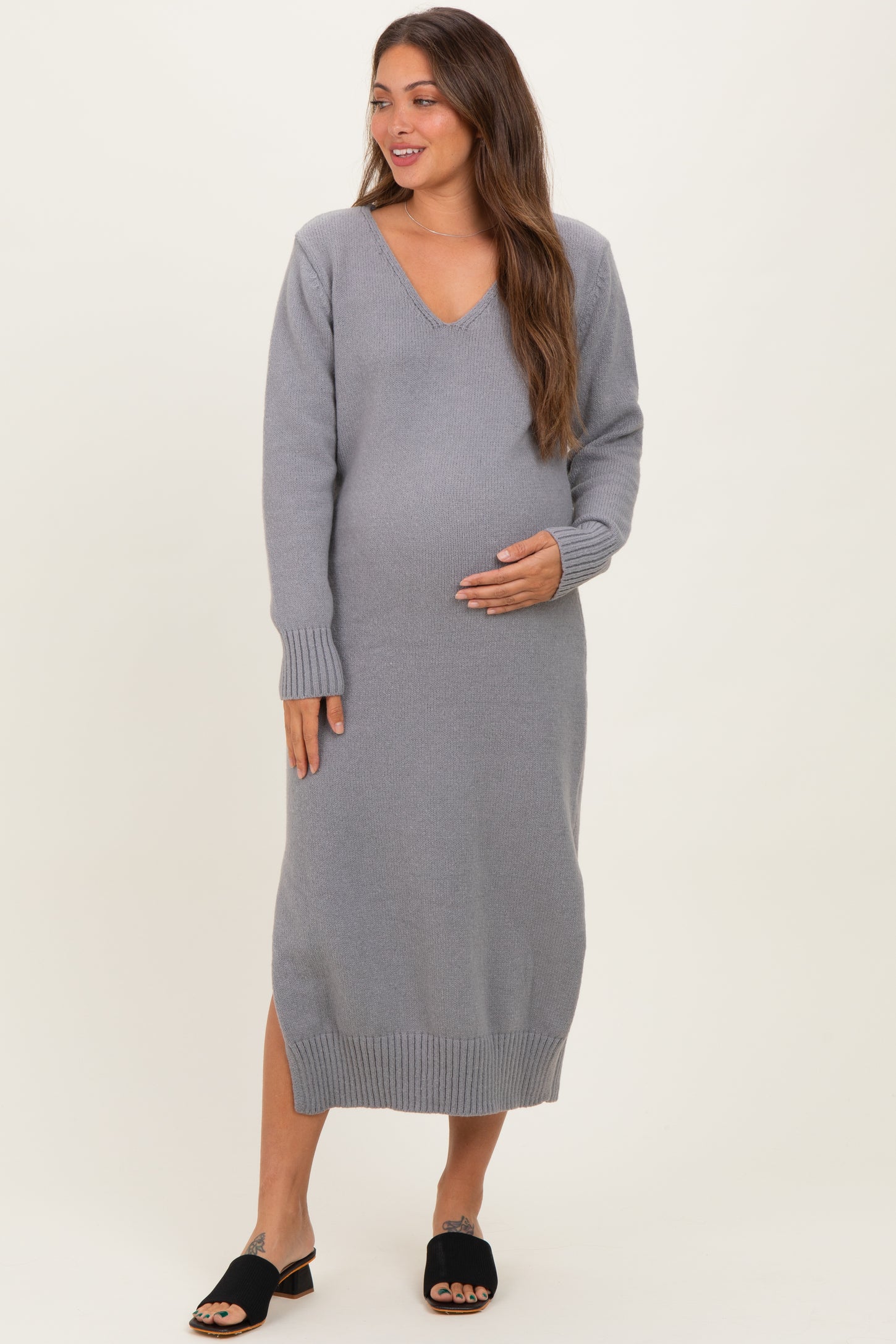woman wearing a gray long sleeve maternity dress with a v-neck and side slits, gently cradling her baby bump