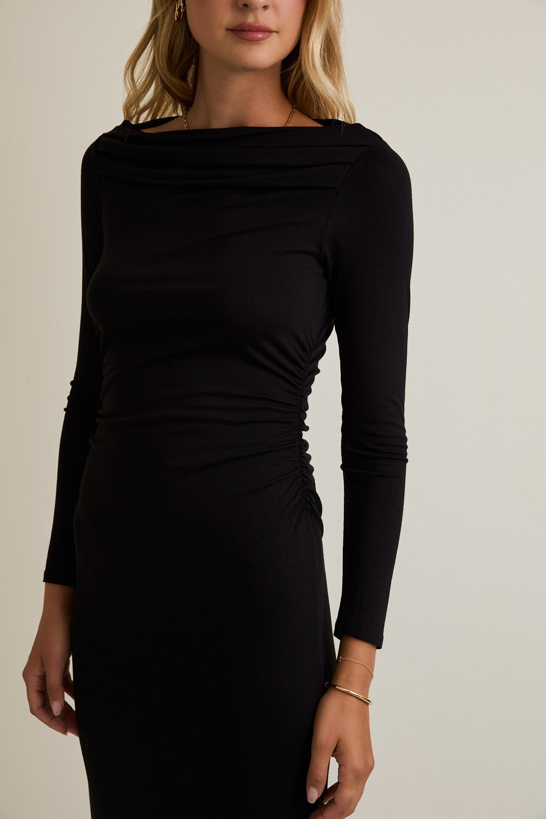 woman wearing a black long sleeve dress with gathered side detailing and a boat neckline