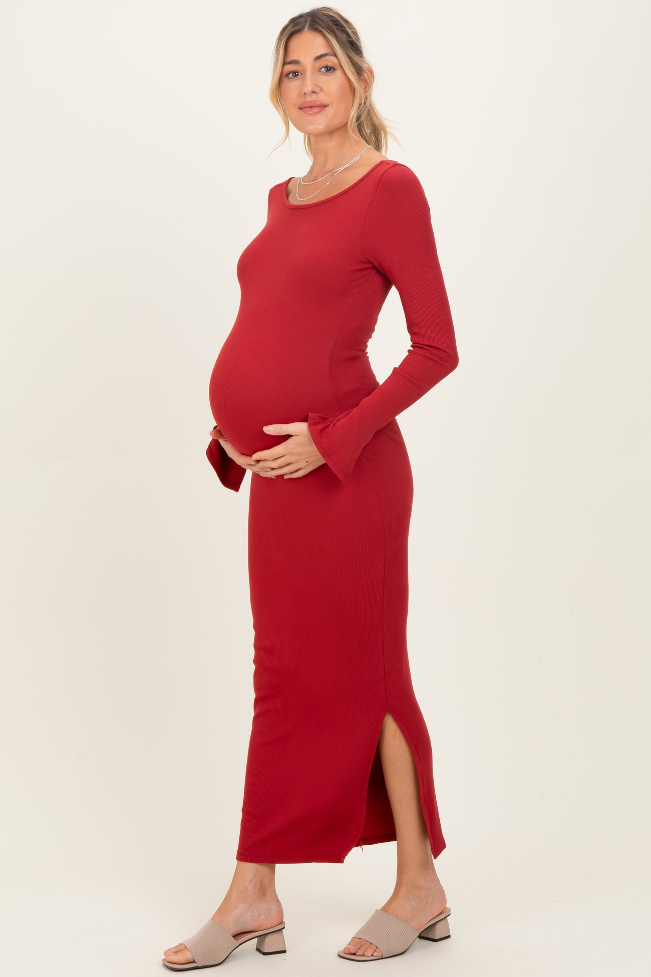 woman wearing a red ribbed maternity dress with side slits and holding her baby bump