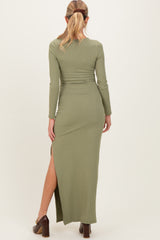 woman wearing a long green ribbed maternity dress with a side slit, showing her back and hair styled in a ponytail