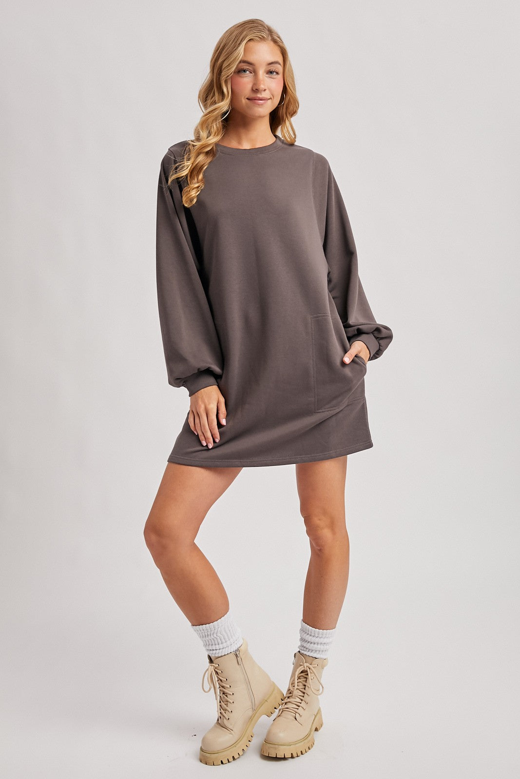 woman wearing a dark gray long sleeve sweatshirt dress with a pocket and styled with tan combat boots