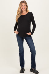 woman wearing a black long sleeve maternity top and blue jeans, with a visible baby bump