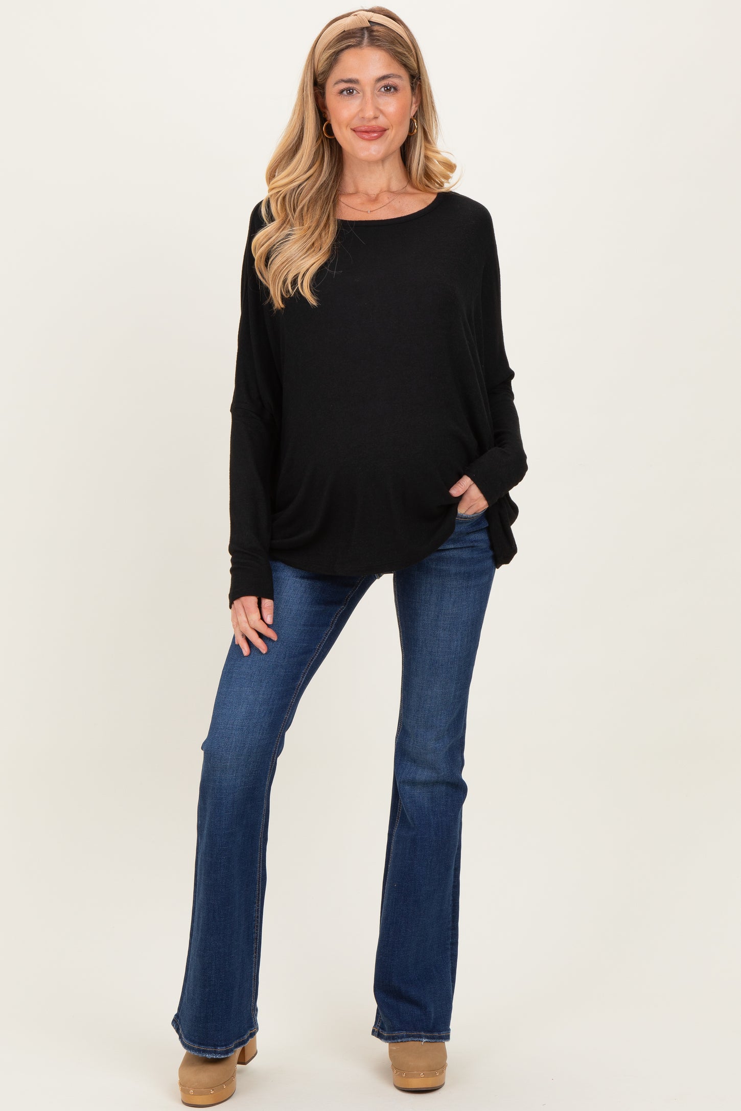 woman wearing a black loose fit maternity top with a baby bump and flared blue jeans