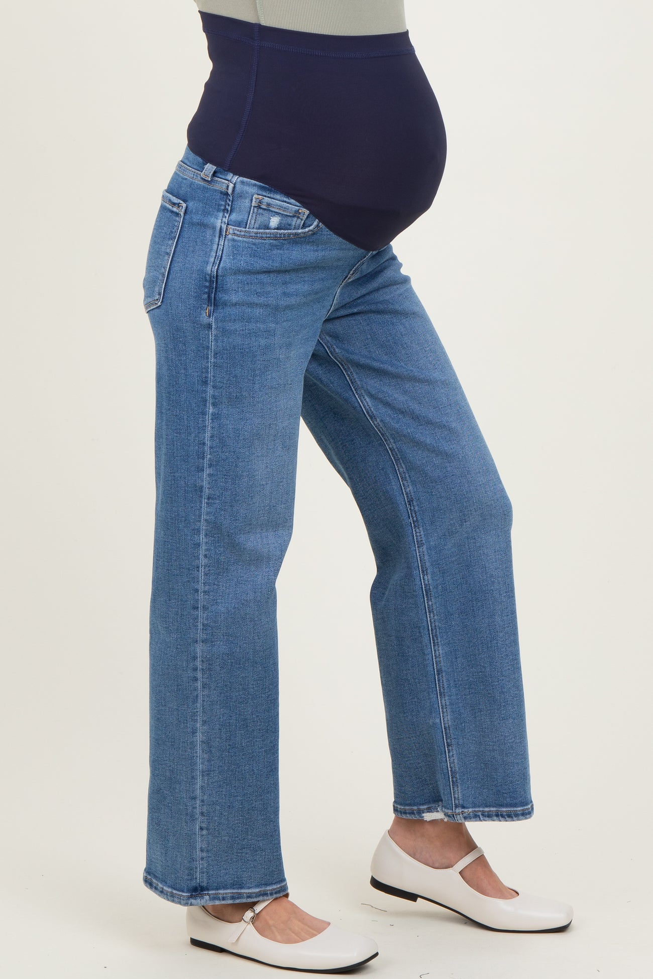 woman wearing light blue maternity jeans with a navy belly band and white flats, highlighting her baby bump