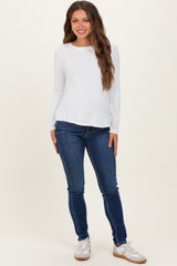 woman wearing a white long sleeve maternity top and blue skinny jeans, showing a baby bump